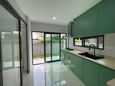 Modern kitchen with green cabinets and large windows for natural light.