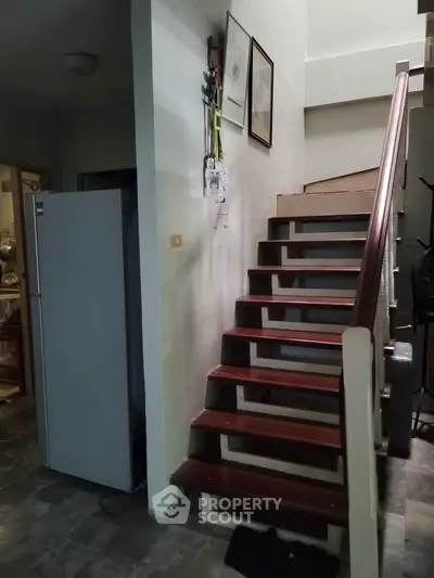 Charming interior staircase with wooden steps and adjacent modern refrigerator, ideal for compact living spaces.