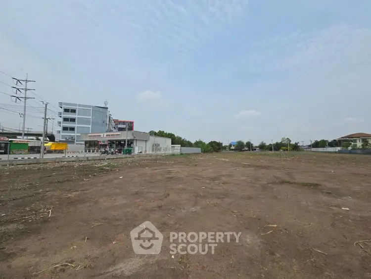 Expansive vacant land plot ideal for development with nearby commercial buildings and clear sky view.