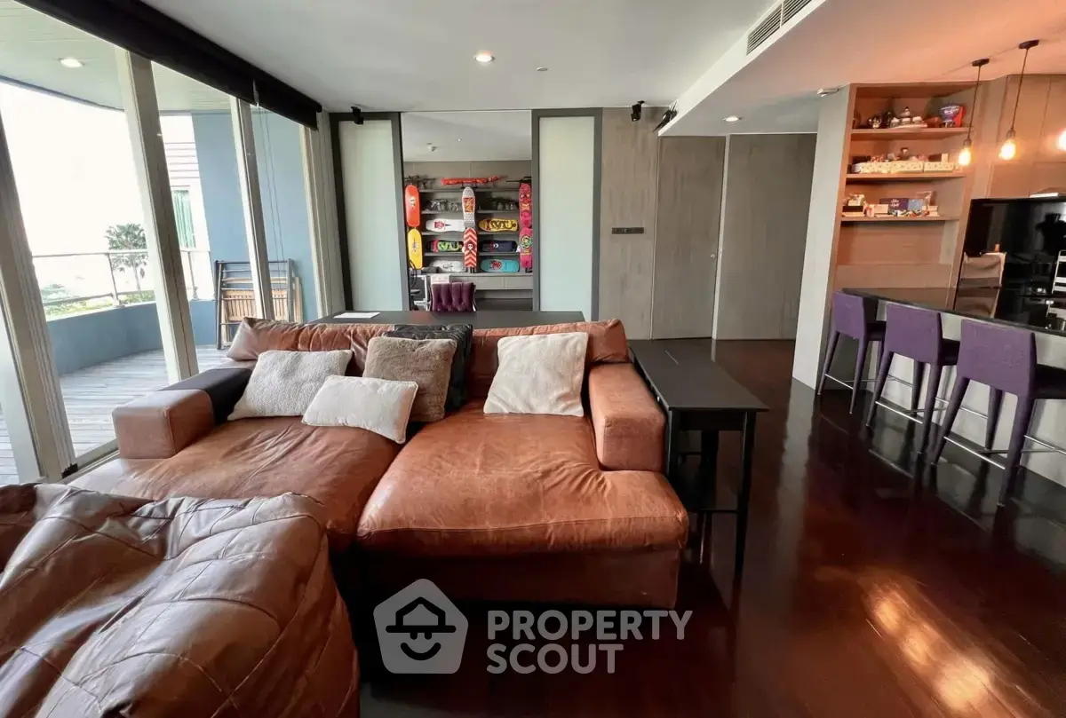 Spacious modern living room with leather sofa and open kitchen, featuring elegant wooden flooring and balcony access.