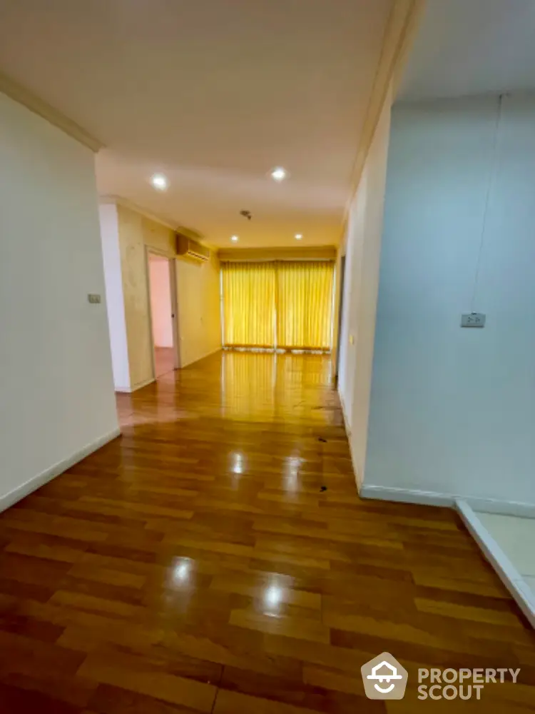 Spacious hardwood floor hallway leading to bright room with large windows