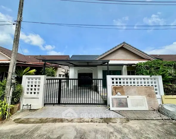 Charming single-story house with gated driveway and lush greenery, perfect for family living.