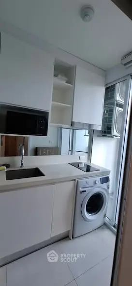 Modern compact kitchen with washing machine and microwave in sleek white cabinetry.