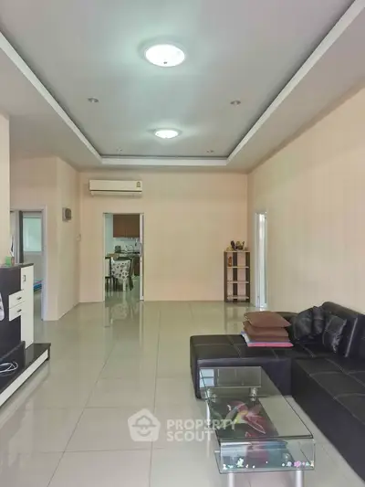 Spacious living room with modern black sofa and glass coffee table, open layout to dining area.