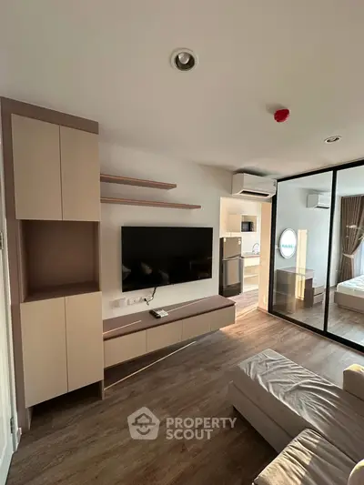 Modern living room with sleek TV setup and open view into bedroom, featuring stylish wood flooring.