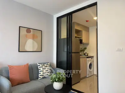 Modern apartment interior with cozy living room and compact kitchen featuring washing machine and fridge.