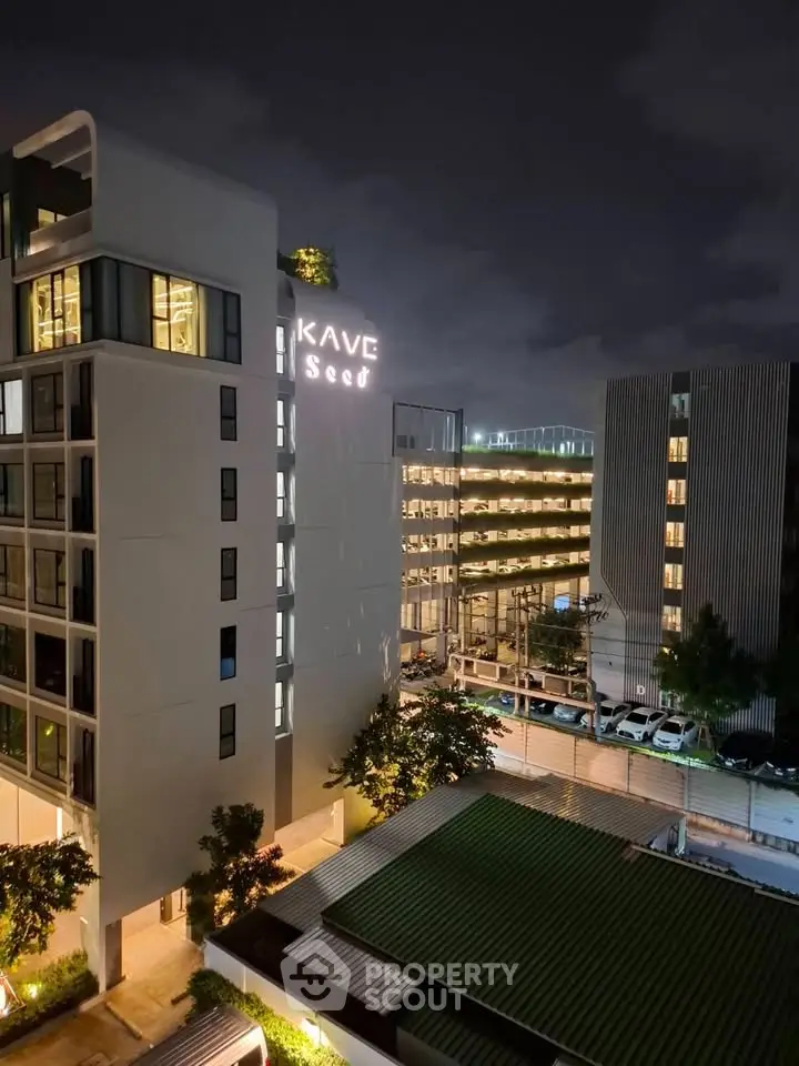 Modern urban apartment building exterior at night with illuminated signage and surrounding cityscape.