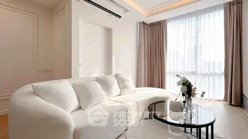 Elegant living room with plush white sofa and modern decor, featuring large windows for natural light.