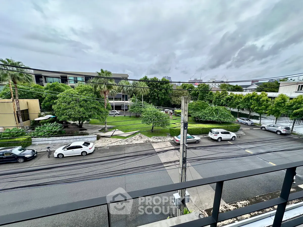 Scenic urban street view from balcony with lush greenery and parked cars.