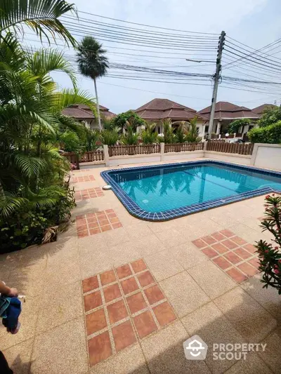 Charming backyard with a sparkling pool surrounded by lush greenery and a tiled patio, perfect for relaxation.