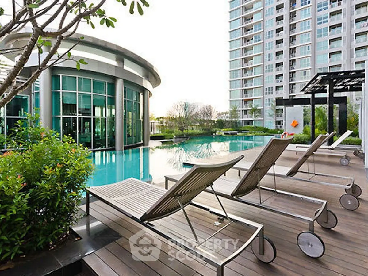 Luxurious condominium pool area with modern lounge chairs and lush greenery.