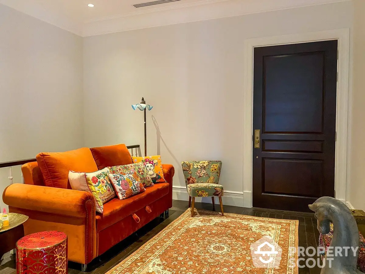 Inviting living room with vibrant orange sofa, eclectic throw pillows, traditional area rug, and elegant dark wood door.