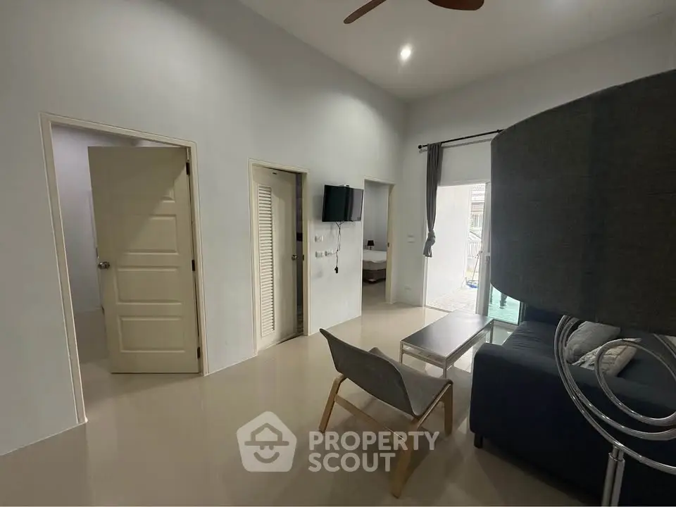Modern living room with sleek furniture and neutral tones, featuring a wall-mounted TV and open doorways.
