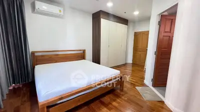 Spacious bedroom with wooden flooring and modern furnishings in a cozy apartment.