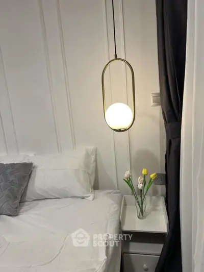 Cozy bedroom with modern pendant light and elegant white bedding, featuring a stylish nightstand with decorative flowers.