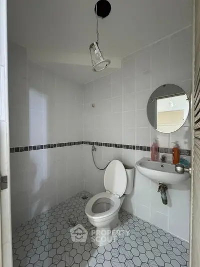Modern bathroom with white tiles and round mirror, featuring a toilet and sink.