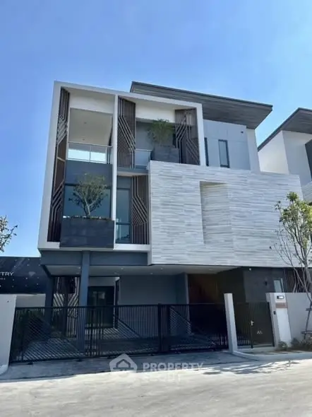 Modern three-story house with sleek design and large windows in a sunny neighborhood.