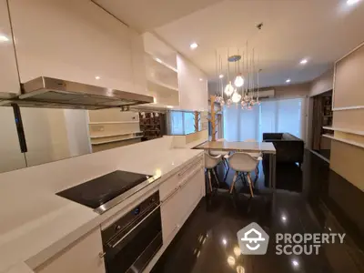 Modern open kitchen with sleek design and dining area, featuring stylish lighting and glossy flooring.