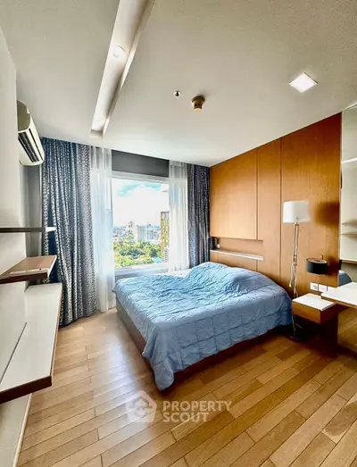 Modern bedroom with large window and city view, featuring wooden flooring and stylish decor.