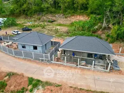 Aerial view of two modern single-story houses with tiled roofs in a serene green setting.