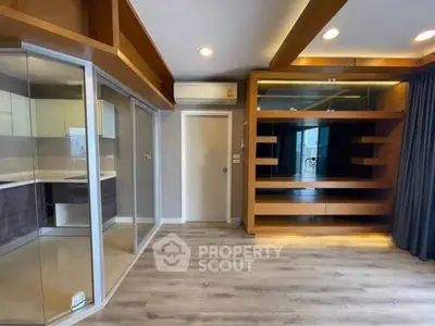 Modern living room with wooden accents and glass partitions, featuring built-in shelving and sleek flooring.