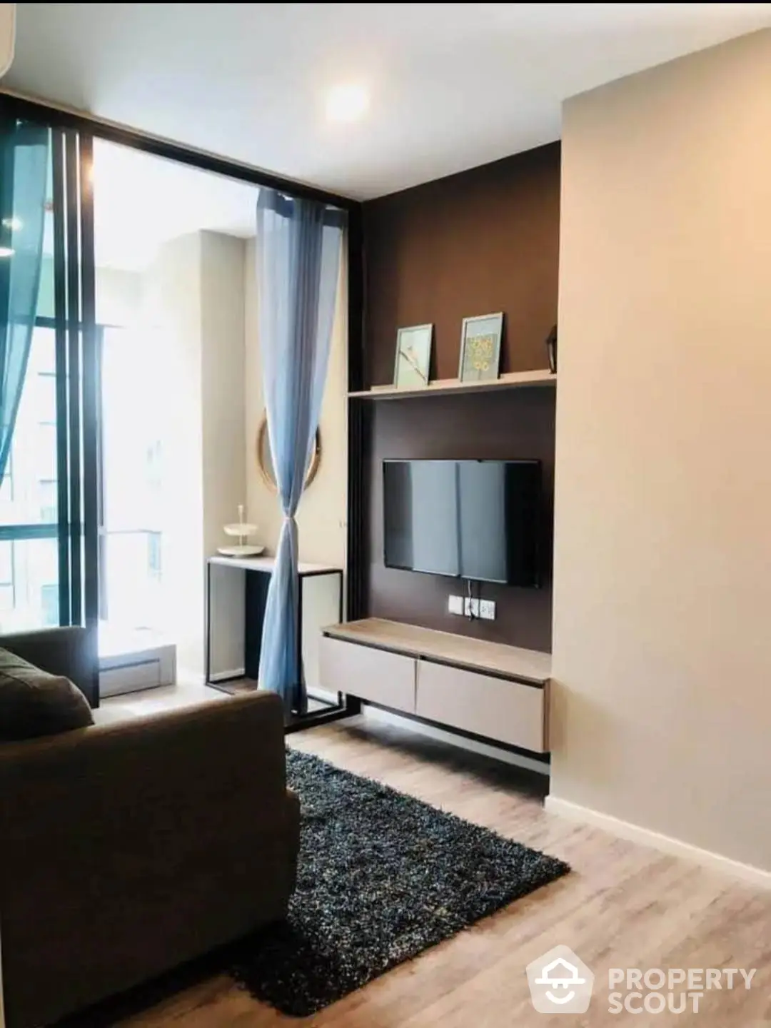 Chic modern living room with sleek entertainment unit, plush sofa, and floor-to-ceiling window allowing natural light to enhance the warm, inviting ambiance.