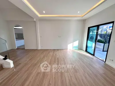 Spacious modern living room with wooden flooring and large glass doors opening to a garden.