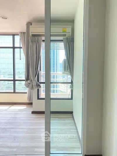 Modern apartment with large windows and city view, featuring sleek flooring and air conditioning.