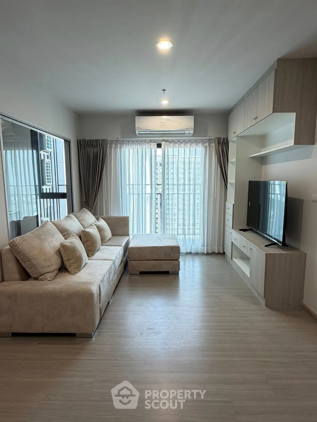 Modern living room with large sofa and entertainment center, featuring floor-to-ceiling windows.