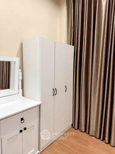 Elegant bedroom with white wardrobe and vanity against beige walls and luxurious curtains.