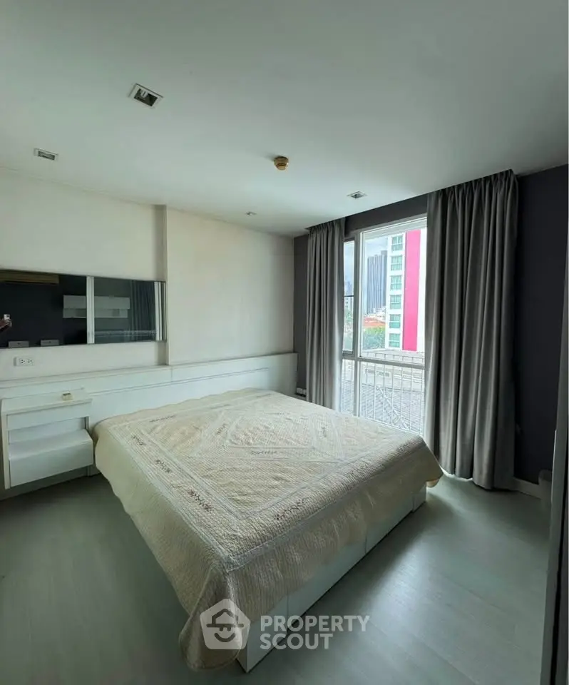 Spacious bedroom with large window and modern decor in a high-rise apartment.