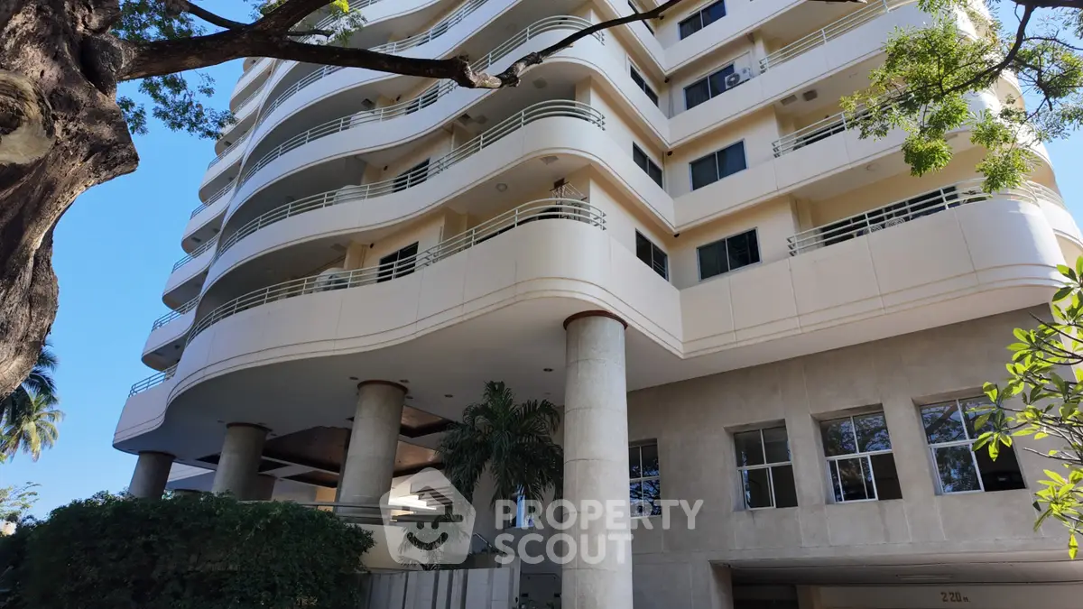 Modern multi-story residential building with curved balconies and lush greenery.