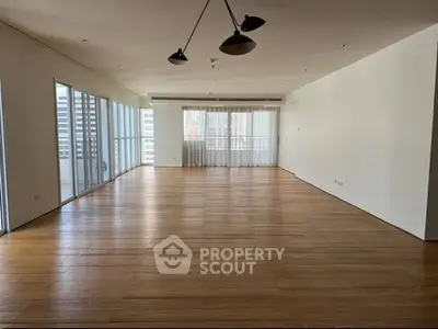 Spacious empty living room with wooden floors and large windows in modern apartment.