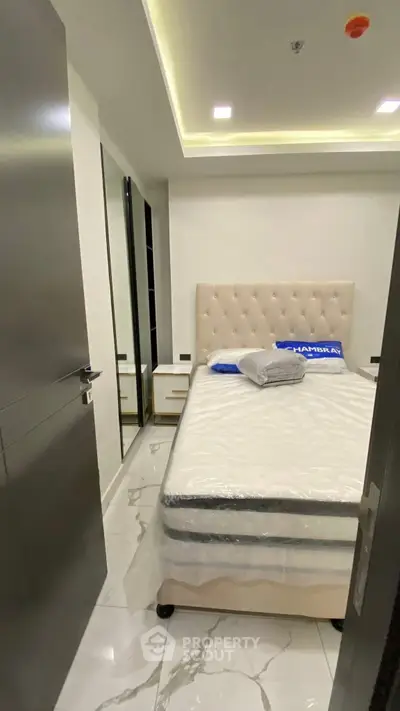 Modern bedroom with plush bed and mirrored wardrobe, featuring sleek design and ambient lighting.