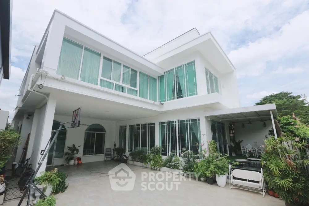 Stunning modern white two-story house with expansive windows and lush greenery