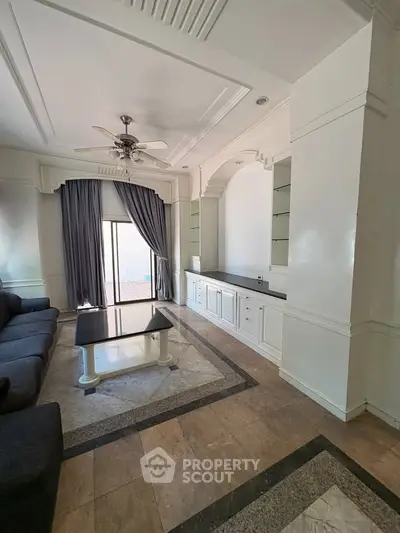 Elegant living room with stylish ceiling fan and large window draped with curtains, featuring a cozy seating area.