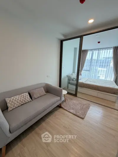 Modern apartment with cozy living room and stylish bedroom separated by glass partition.