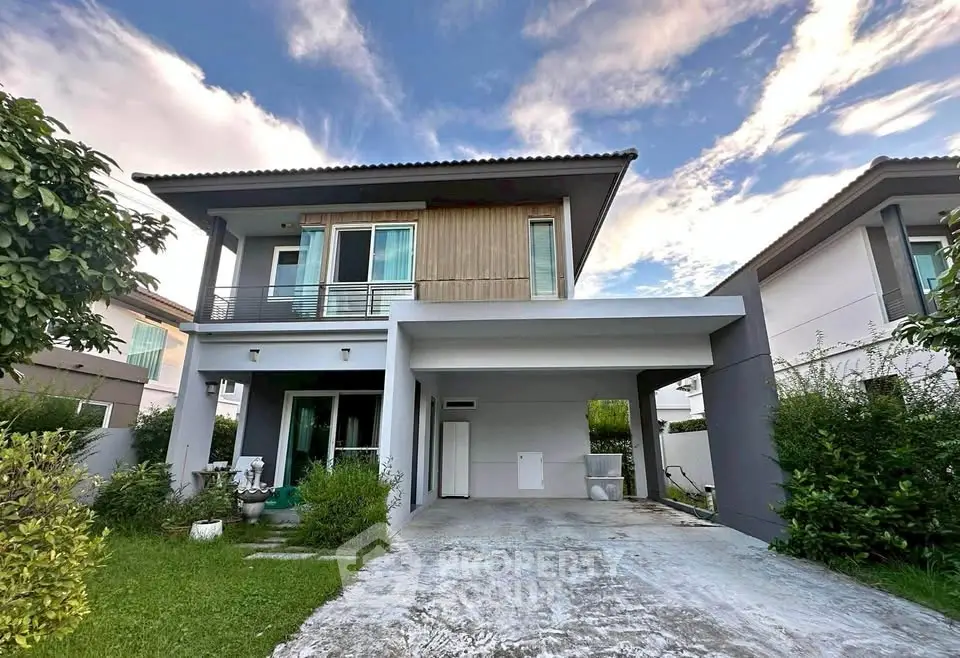 Modern two-story house with spacious driveway and lush green garden under a clear blue sky.
