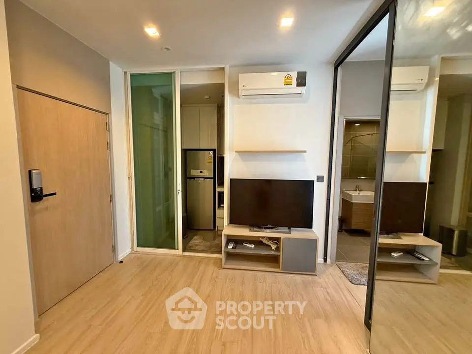 Modern living room with sleek wooden flooring, wall-mounted TV, and mirrored wardrobe in a stylish apartment.