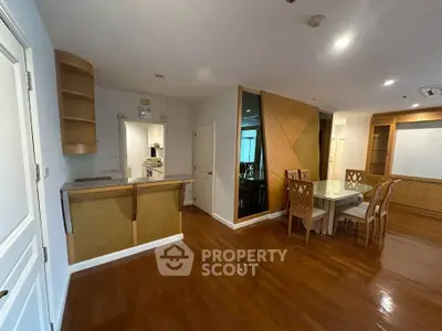 Spacious dining area with elegant wooden flooring and modern kitchen in open layout apartment.