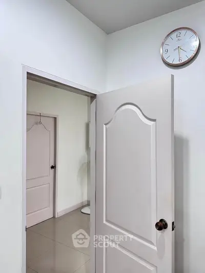 Minimalist interior with open door and wall clock, showcasing modern design and clean lines.