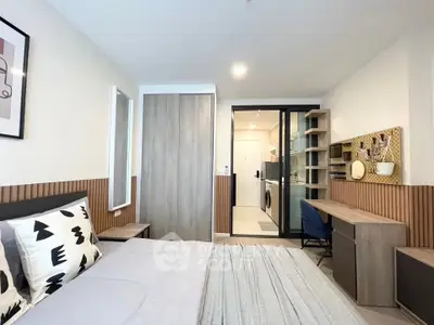 Modern bedroom with stylish decor and workspace, featuring a sliding door to a compact kitchen area.