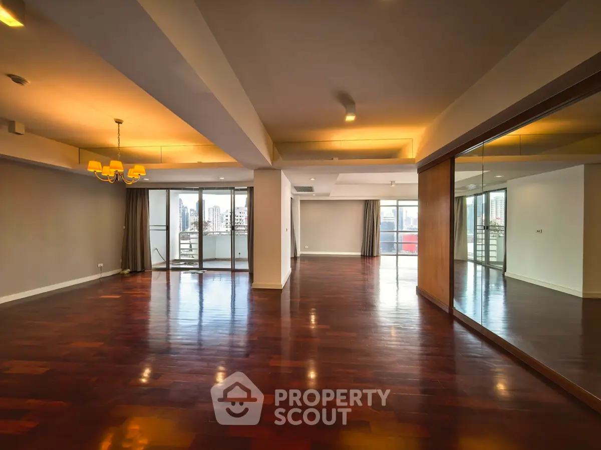 Spacious modern living room with hardwood floors and large windows offering city views.