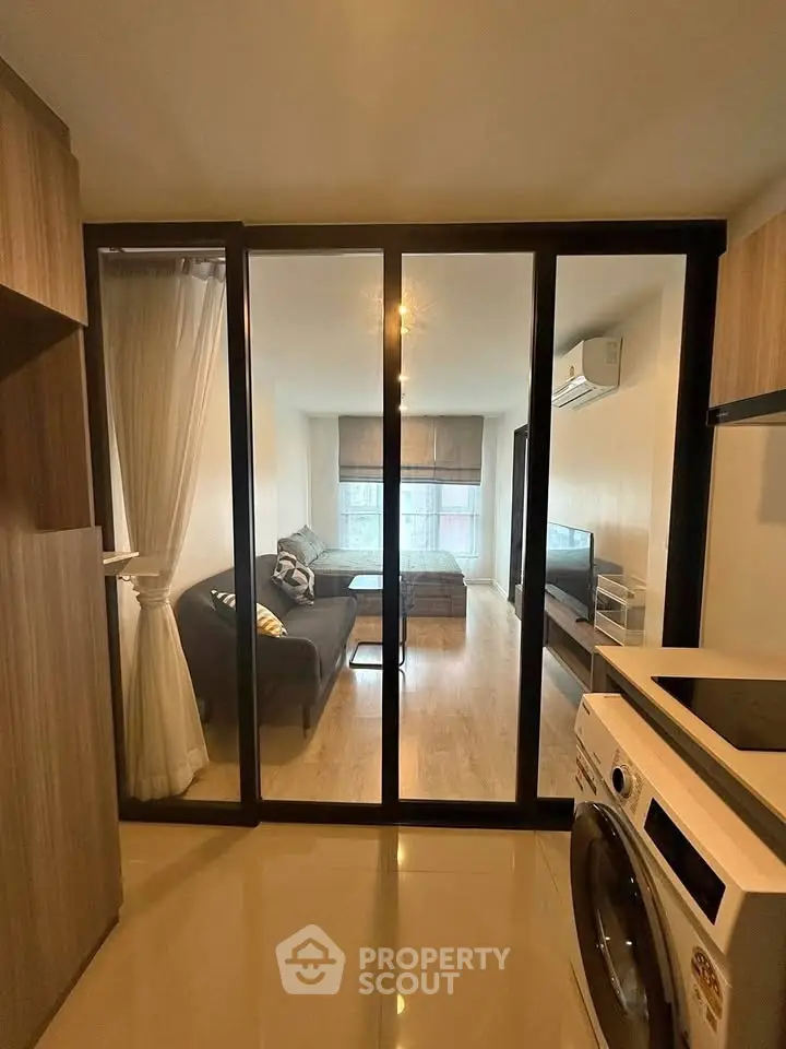 Modern living room with glass partition and washing machine, featuring sleek design and natural light.