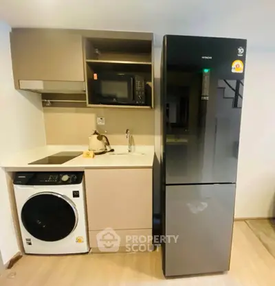 Modern compact kitchen with fridge, microwave, and washing machine in stylish apartment.