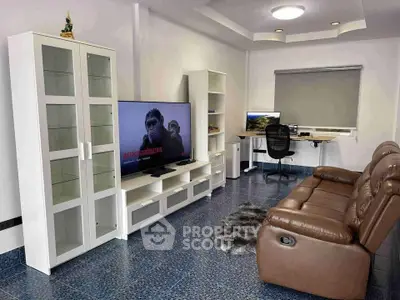Modern living room with sleek furniture and home office setup, featuring a comfortable leather sofa and large TV.