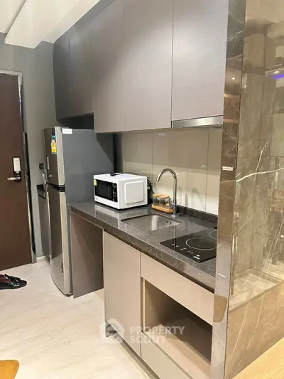 Modern kitchen with sleek cabinets, microwave, and induction cooktop in a compact layout.