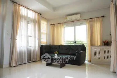 Spacious living room with large windows and elegant curtains, featuring a black leather sofa and modern decor.