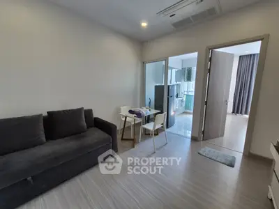 Modern living room with sleek sofa and dining area leading to a bright kitchen.