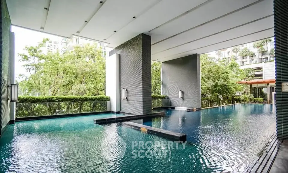 Luxurious modern pool area with sleek design and lush greenery in upscale residential complex.
